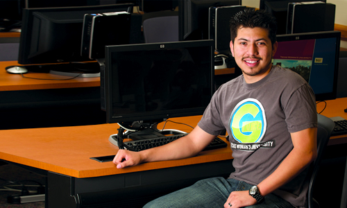 photo of a male student at TWU sitting in a TWU classroom beside a computer