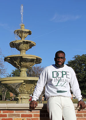 TWU graduate in white sweatshirt leans in front of TWU fountain