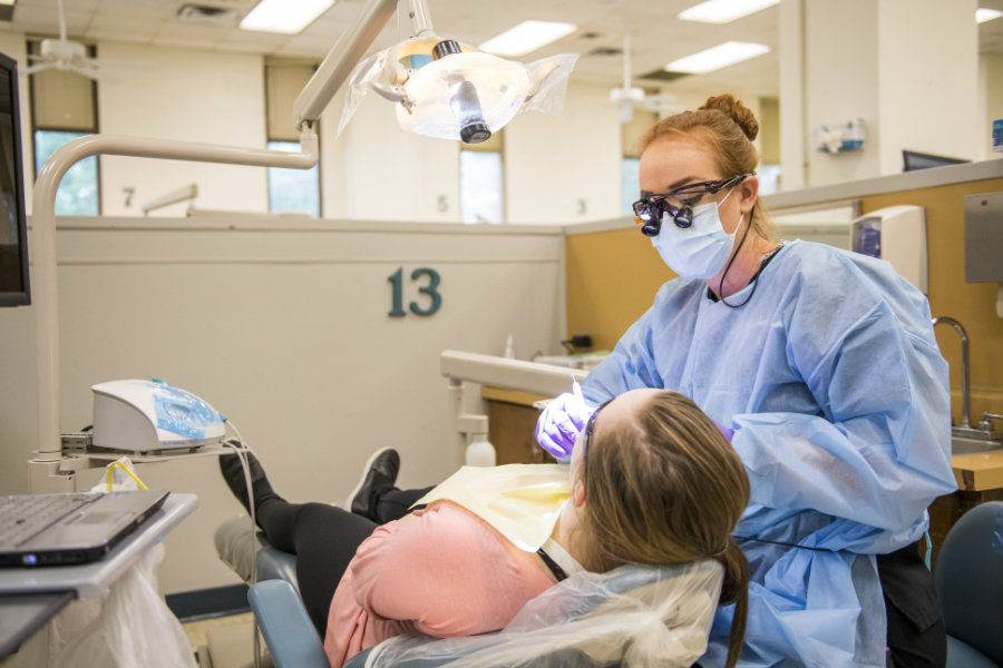 A TWU student in a dentists office setting cleans a patients teeth.
