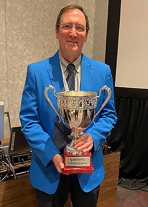 Mark Weber, dressed in blue suit jacket, holds trophy