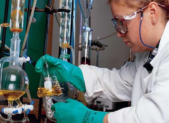 Female wearing a lab coat, safety goggles and gloves, while working in a lab.