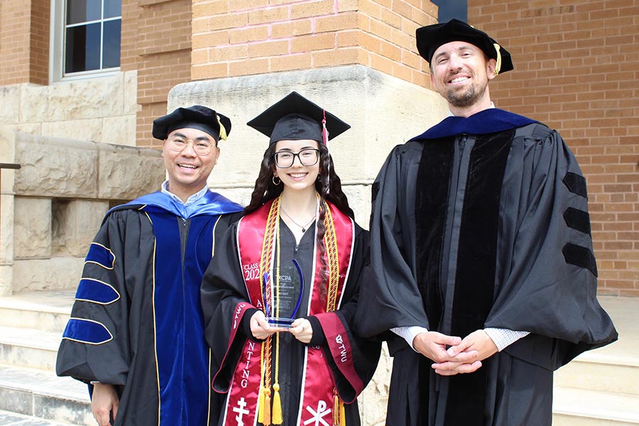 TWU student in graduation attire stands with two faculty members in graduation robes