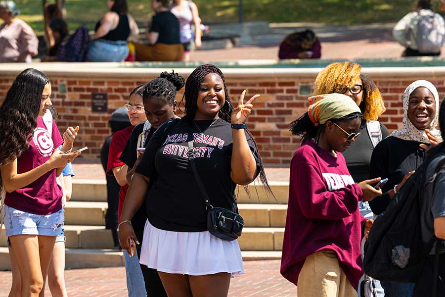  A TWU student at a busy events holds up a peace sign and smiles at the camera.