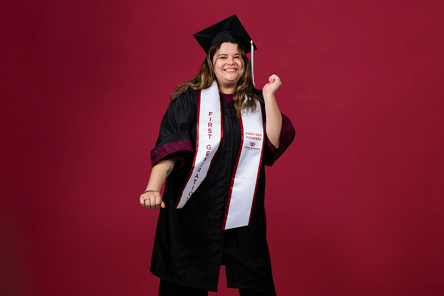 A portrait of a TWU student on a dramatic background in academic regalia and doing a mid-celebration pose.