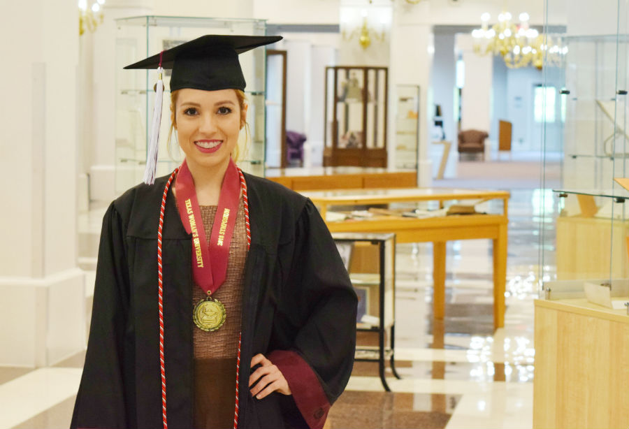 Daisy Cantu standing in the library with a graduation gown.