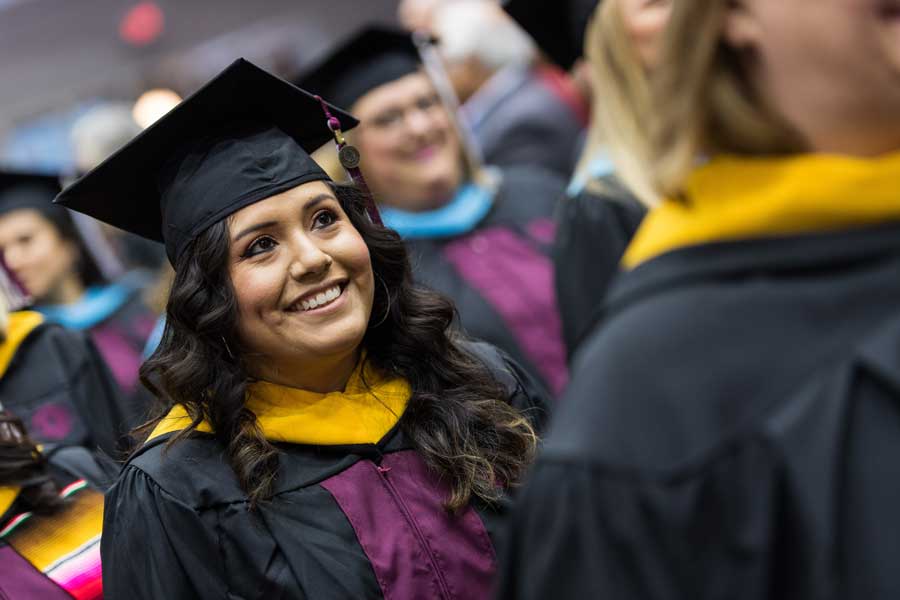 A woman smiles in academic regalia during a TWU commencement ceremony.	