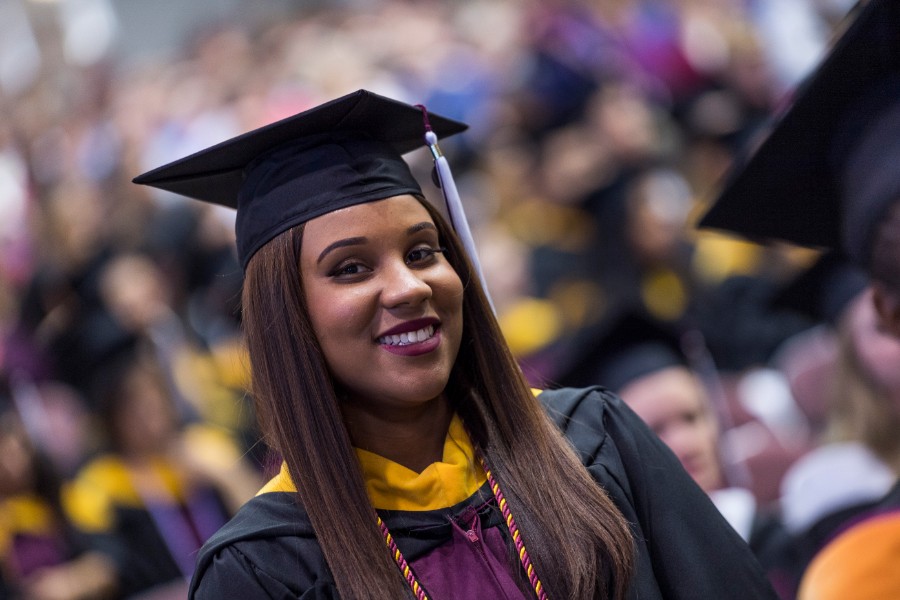 A young African American woman smiling at commencement in her academic regalia.