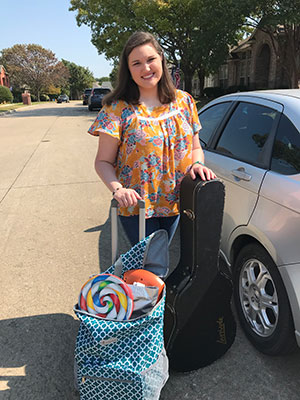 Laurel Page stands beside a car with a rolling cart filled with her music therapy supplies.