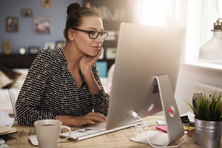 A woman works in an office setting on a Mac computer.