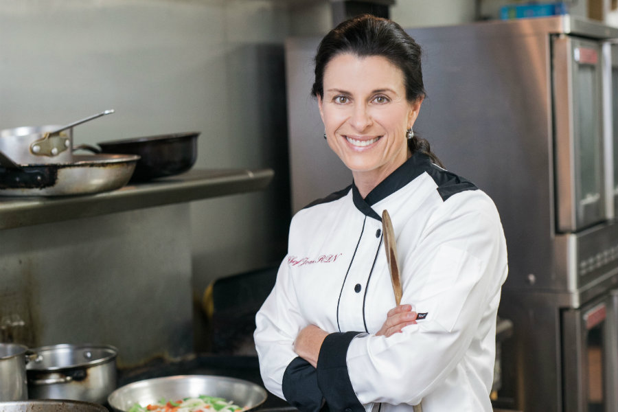 Joan Denton in a chef uniform and posing in a professional kitchen setting