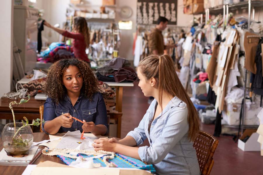 Two women business owners consult together at a table as others work in the background