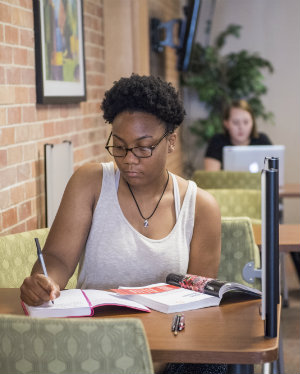 A student in a library setting studying her textbook and taking notes.