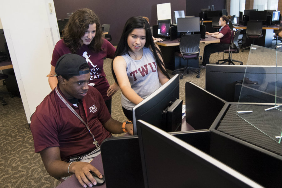 Three students working together in a computer lab setting.