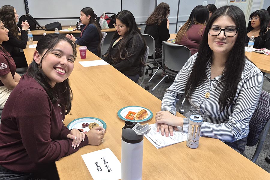 two students sit opposite one another at a table with a plate of food in front of them