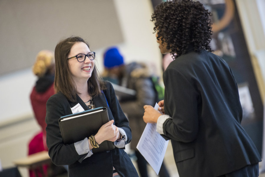 A young woman in business casual talks with a potential employer at a job fair