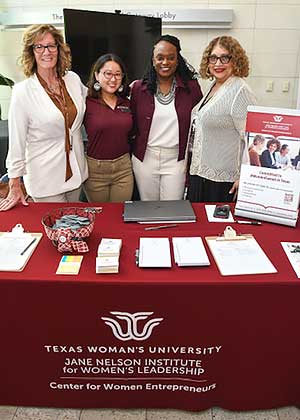 four women stand behind a maroon TWU table at a conference