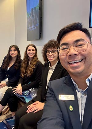 faculty professor takes a selfie with three students sitting next to him