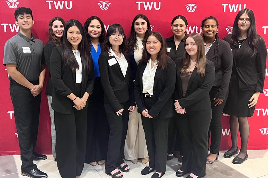 a group of business students in suits stand in front of a maroon backdrop