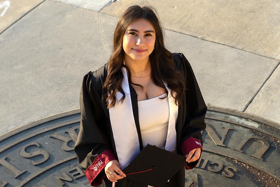 Romina-Vargas-Trujillo in graduation attire standing on the TWU seal