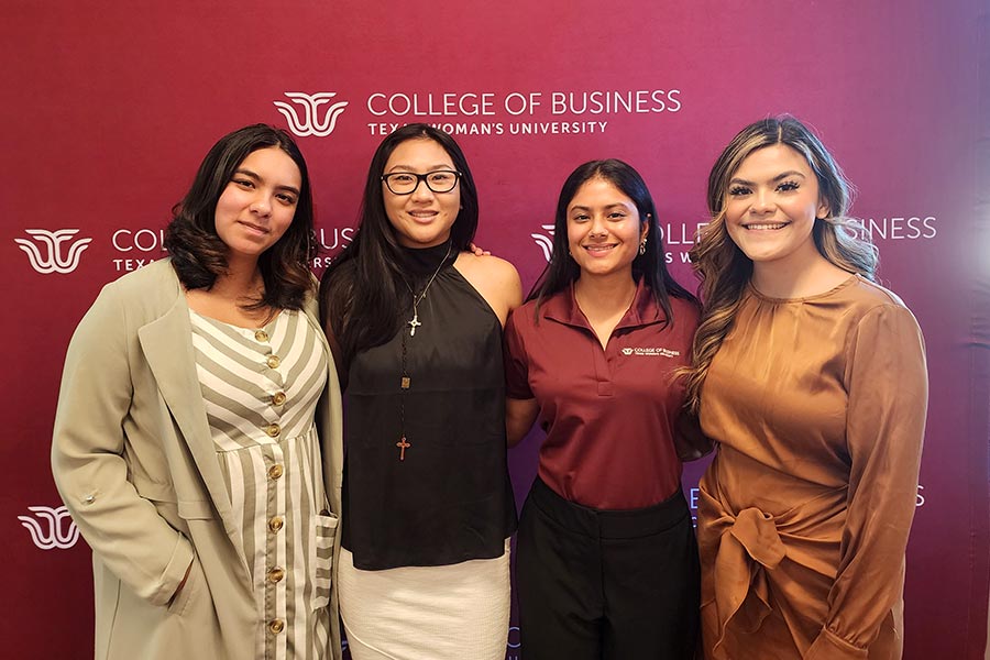 four TWU students stand in front of a maroon College of Business backdrop