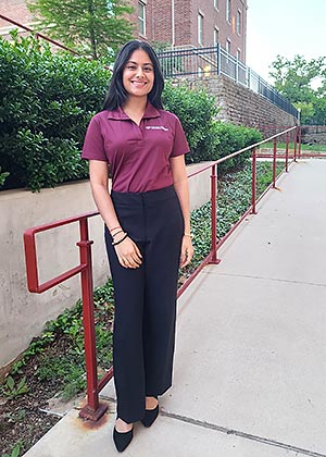 a TWU student in maroon polo and black pants stands in front of a walkway