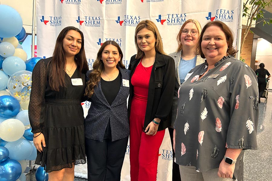 Faculty advisor and four students stand in front of a Texas SHRM white backdrop