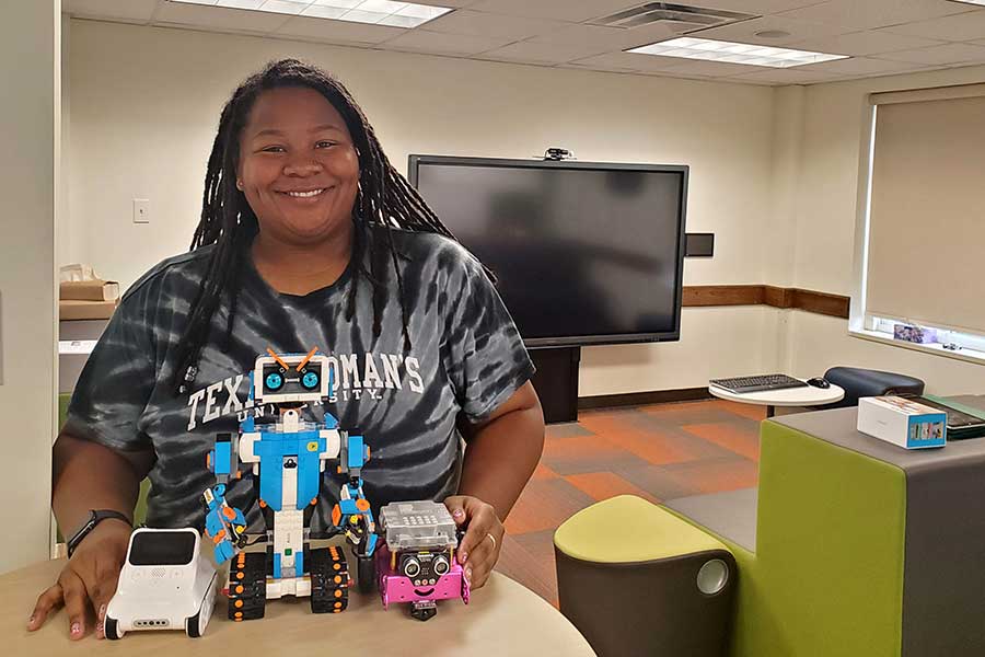 student stands behind desk with small robotics in front of her