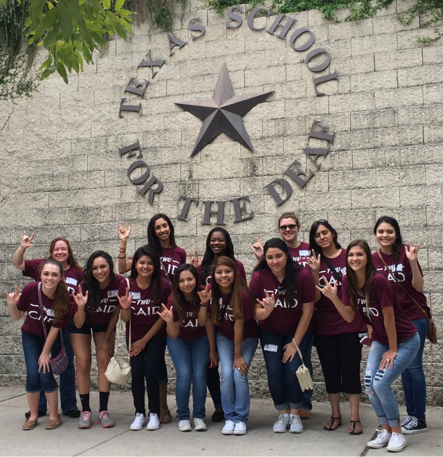 Group of smiling students in front of Texas School for the Deaf sign.