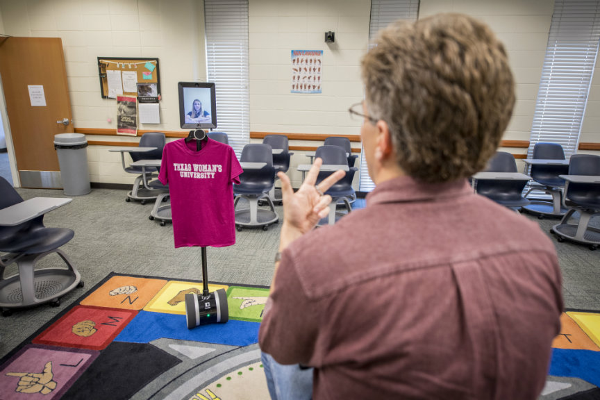 man uses sign language in front of ipad with student on it