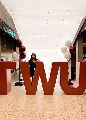 woman in black scrubs behind the large W amid the TWU sign