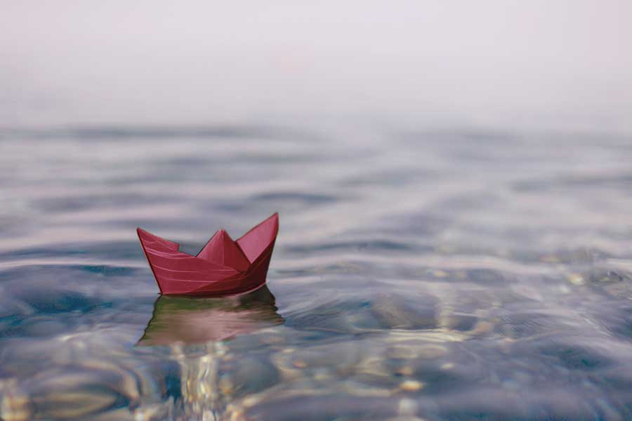 A maroon paper boat floats on water.