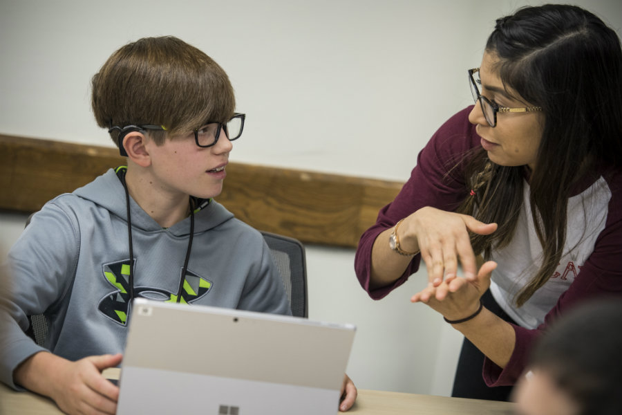 A TWU student and a young boy wearing a hearing aid talk in sign language.