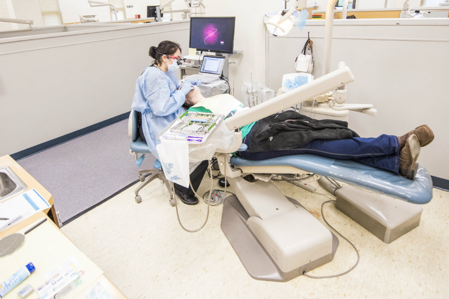 A dentists office setting where a TWU student is working on a patient's teeth in a dentists chair.