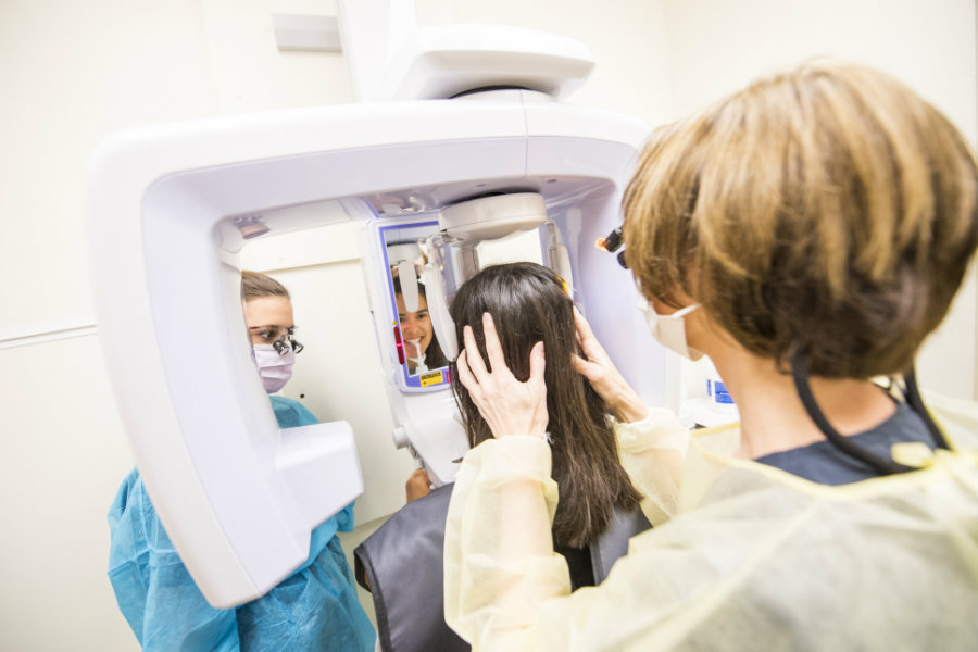 A TWU professor assists a student with taking teeth X-rays with a patient in a dentists office setting.