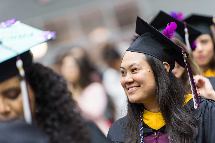 A TWU graduate smiling at commencement with a purple feather on her cap.