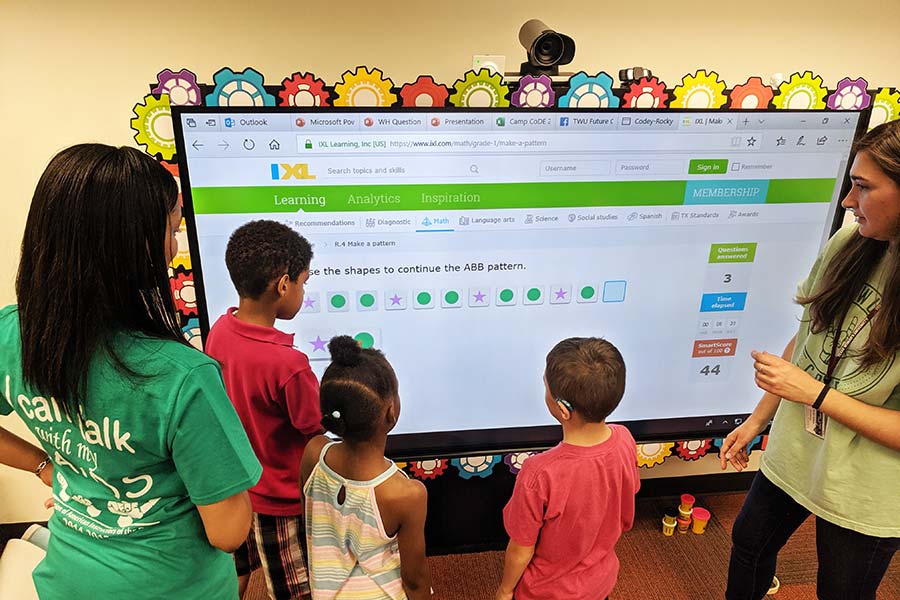 Instructors teach a group of children gathered around a large screen in TWU's Future Classroom Lab