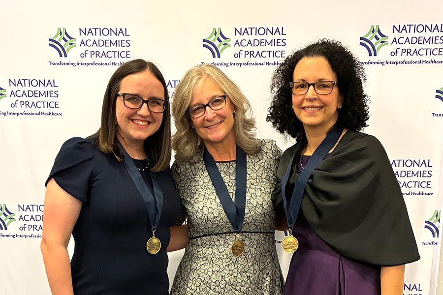 three staff members stand in front of a NAP backdrop with medals around their necks