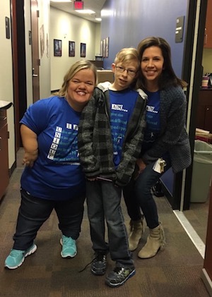 Two women and a boy pose in a school hallway.