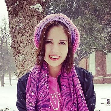 Daisy standing in the snow on campus wearing a wool hat and scarf