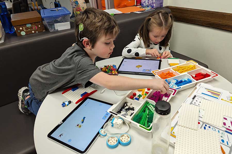 two children play with legos and ipads while sitting next to table