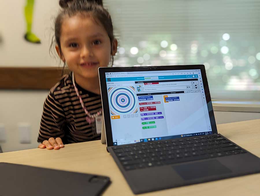 student stands behind laptop that shows coding lesson