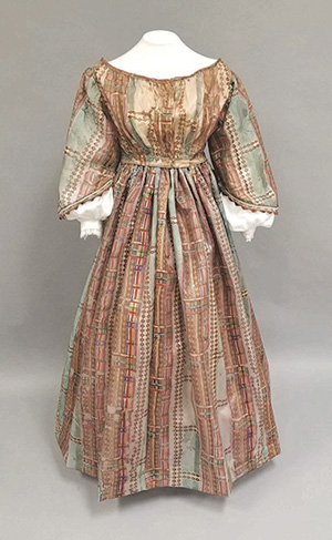 Made of silk French gauze, the gown is light blue and varied colored plaid with bell-shaped sleeves.