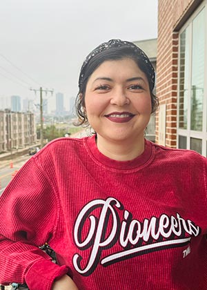 a student, wearing a maroon Pioneers sweatshirt, standing outside on a balcony 