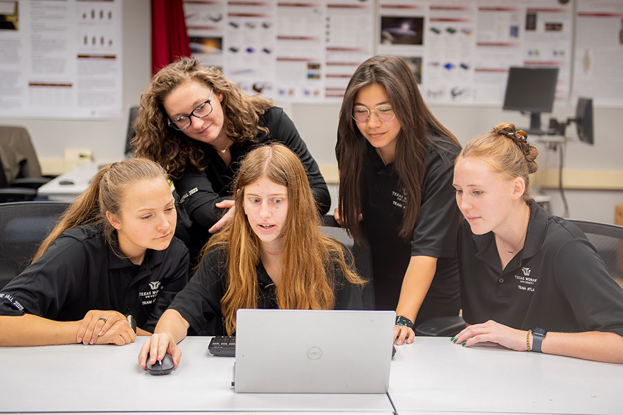 a kinesiology student works on a computer while two students stand behind her and two more sit next to her