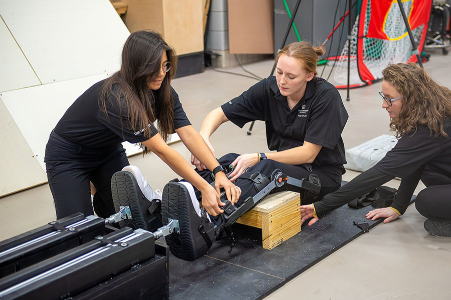 two kinesiology students help student strap into exercise device