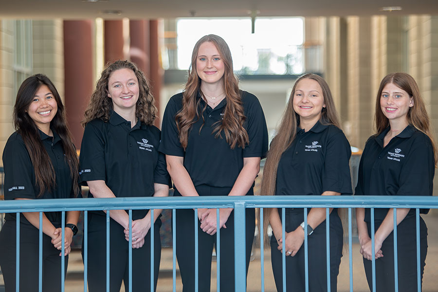 five students in black attire stand behind Pioneer Hall balcony