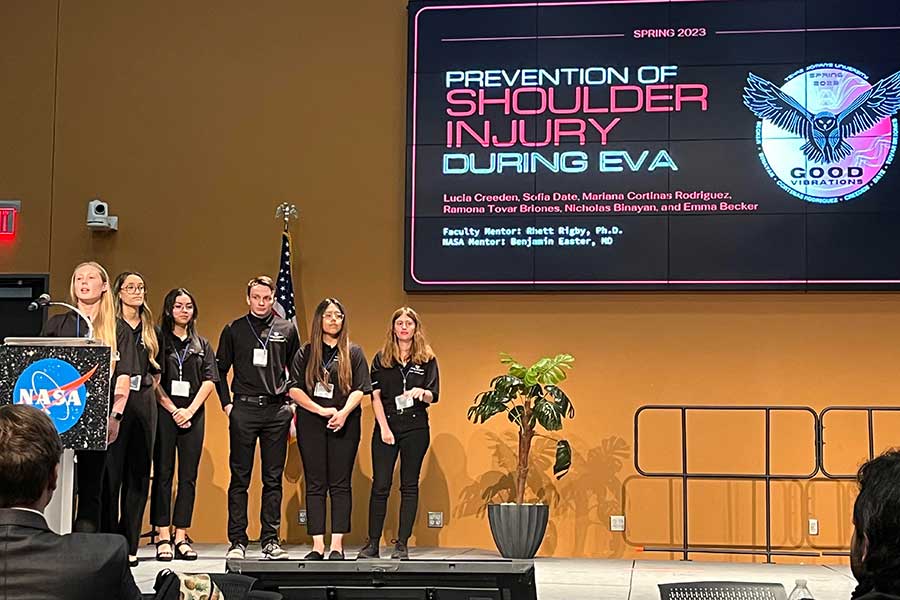 six kinesiology students dressed in black stand on stage in front of large monitor