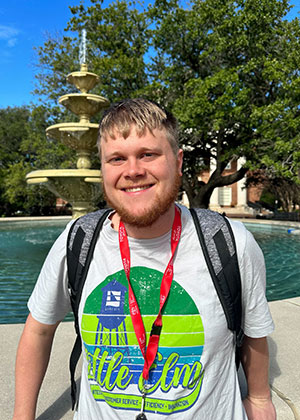 TWU and Transition Academy student standing with backpack standing in front of the TWU fountain