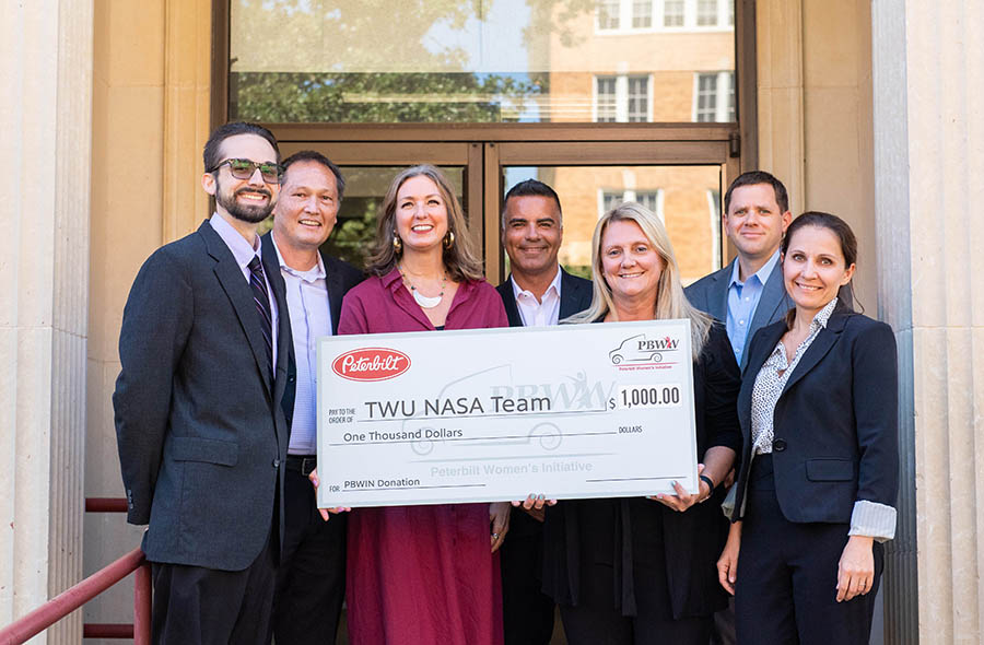 seven faculty stand in front of doorway with large check