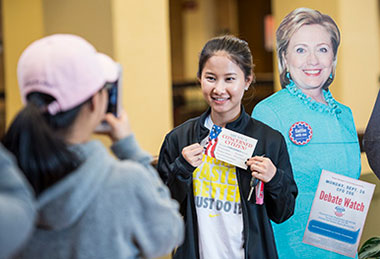 Student taking a photo next to a life-size cutout of Hillary Clinton